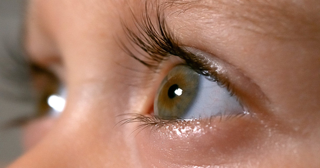A close-up of a watery eye with long lashes, the lower lid wet with tears